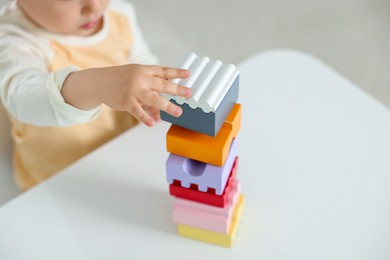 Photo of Cute little child playing with building bricks at white table indoors, closeup