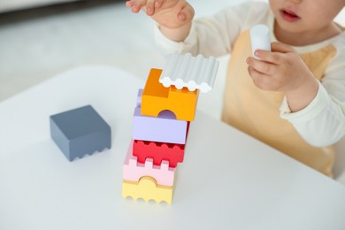 Photo of Cute little child playing with building bricks at white table indoors, closeup