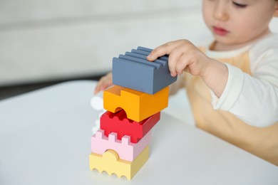 Photo of Cute little child playing with building bricks at white table indoors, closeup