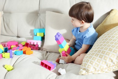 Photo of Cute little child playing with building bricks on sofa at home