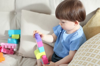Photo of Cute little child playing with building bricks on sofa at home
