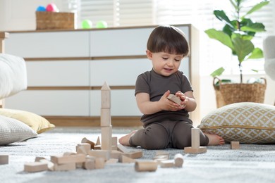 Photo of Cute little child playing with wooden building blocks at home. Space for text