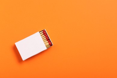 Photo of Matches in box on orange background, top view. Mockup for design