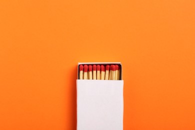 Photo of Matches in box on orange background, top view. Mockup for design