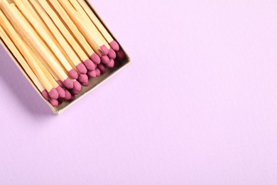 Photo of Matches in open box on violet background, top view. Space for text