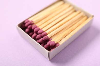 Photo of Matches in open box on violet background, closeup
