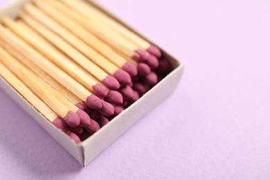 Photo of Matches in open box on violet background, closeup
