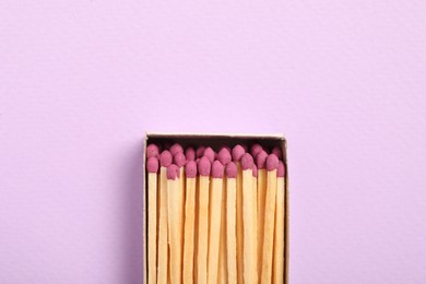 Photo of Matches in open box on violet background, top view. Space for text