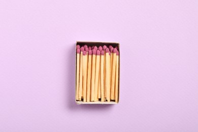 Photo of Matches in open box on violet background, top view