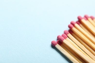 Photo of Matches with pink heads on light blue background, closeup. Space for text