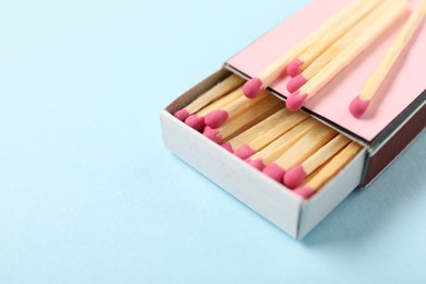 Photo of Matches and box on light blue background, closeup. Space for text