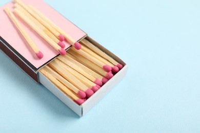 Photo of Matches and box on light blue background, closeup. Space for text