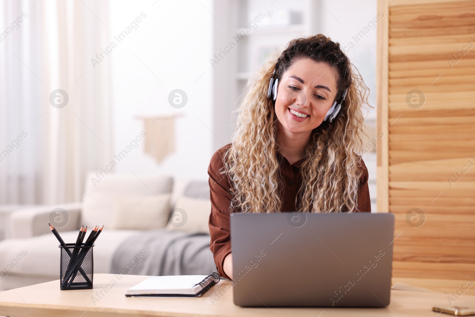 Smiling woman in headphones working with laptop at desk in home office Photo of Smiling woman in headphones working with laptop at desk in home office