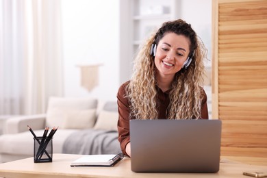 Photo of Smiling woman in headphones working with laptop at desk in home office