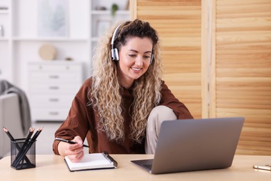 Photo of Smiling woman in headphones working with laptop at desk in home office