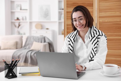 Photo of Smiling woman having videochat by laptop at desk in home office