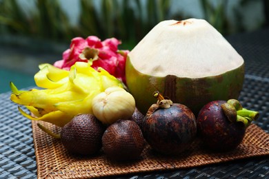 Photo of Different tropical fruits on wicker table, closeup