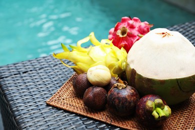 Photo of Different tropical fruits on wicker table near swimming pool, closeup. Space for text