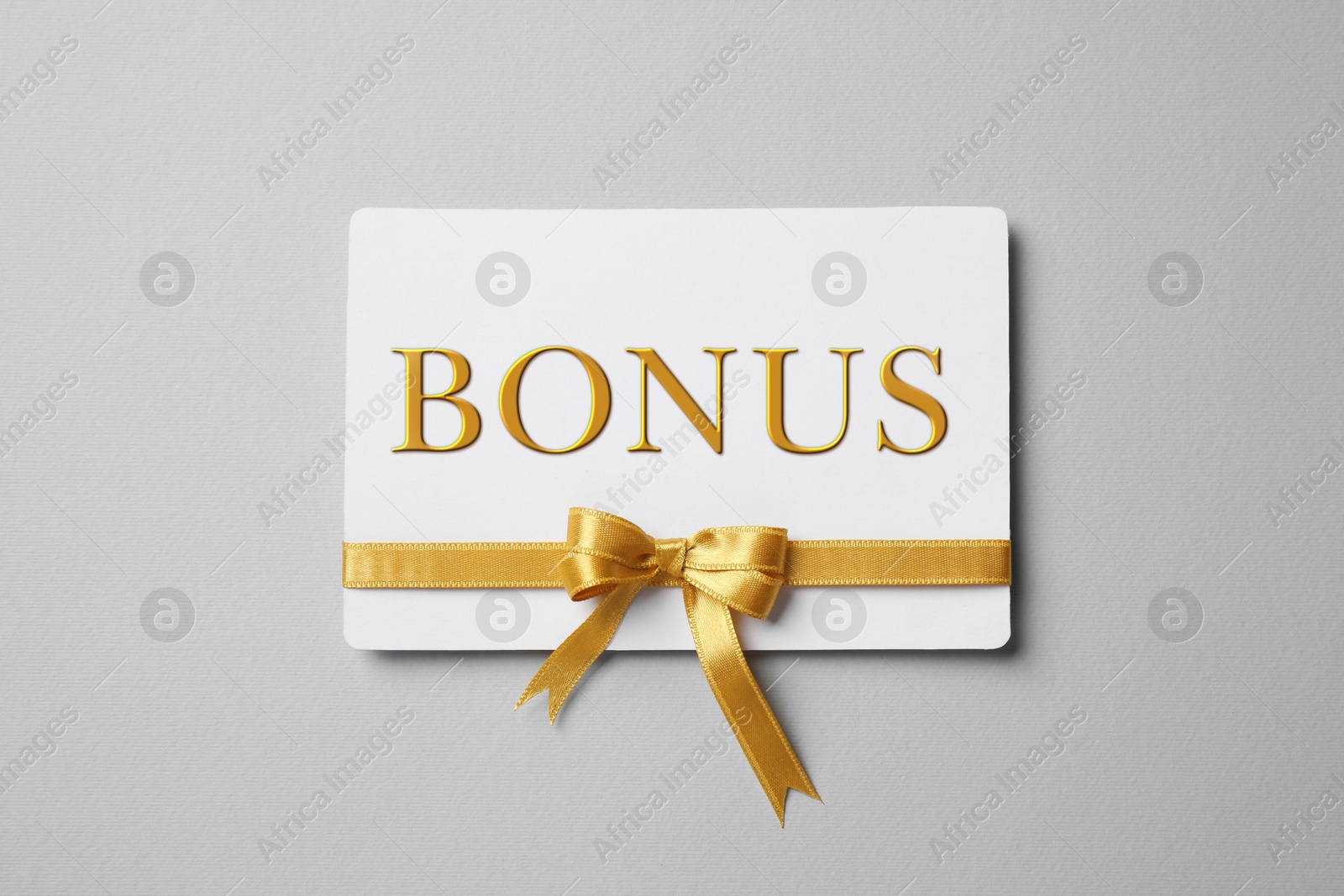 Bonus card with golden bow on grey background, top view Image of Bonus card with golden bow on grey background, top view