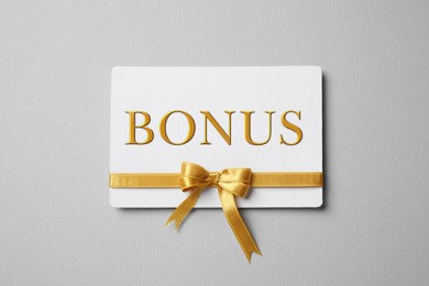 Image of Bonus card with golden bow on grey background, top view