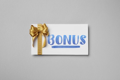 Image of Bonus card with golden bow on grey background, top view