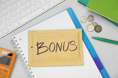 Image of Envelope with word Bonus, coins, calculator and notebook on white office table, flat lay