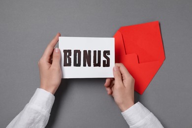 Image of Woman holding card with word Bonus at grey table, top view