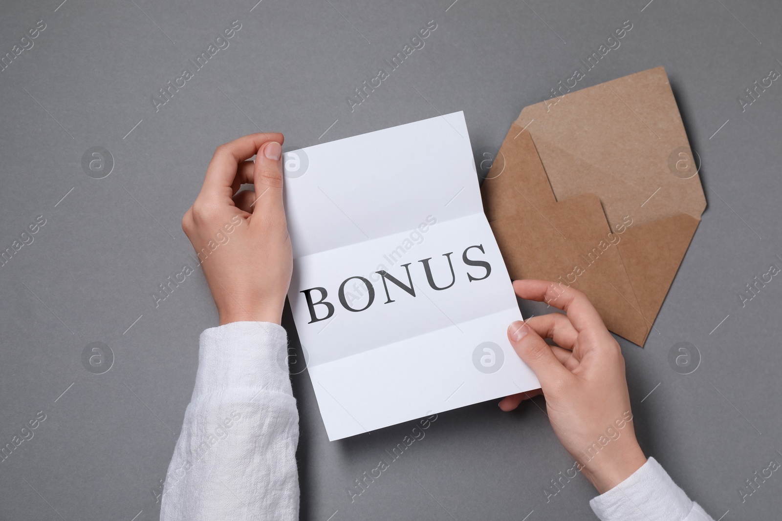 Woman holding paper with word Bonus at grey table, top view Image of Woman holding paper with word Bonus at grey table, top view