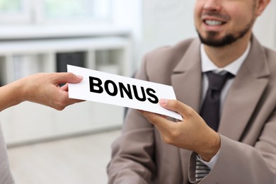 Image of Smiling employee receiving envelope with bonus from boss in office, closeup