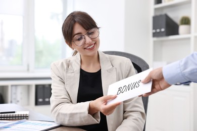 Image of Smiling employee receiving envelope with bonus from boss in office
