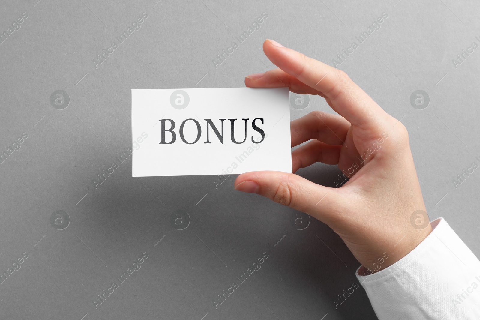 Woman holding card with word Bonus at grey table, top view Image of Woman holding card with word Bonus at grey table, top view