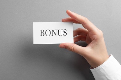Image of Woman holding card with word Bonus at grey table, top view