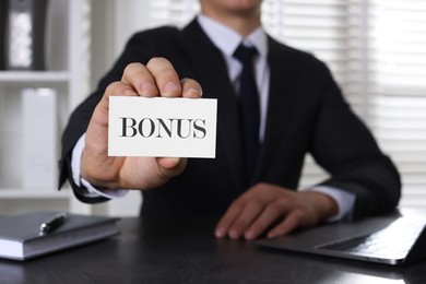 Image of Businessman showing card with word bonus at table in office, closeup