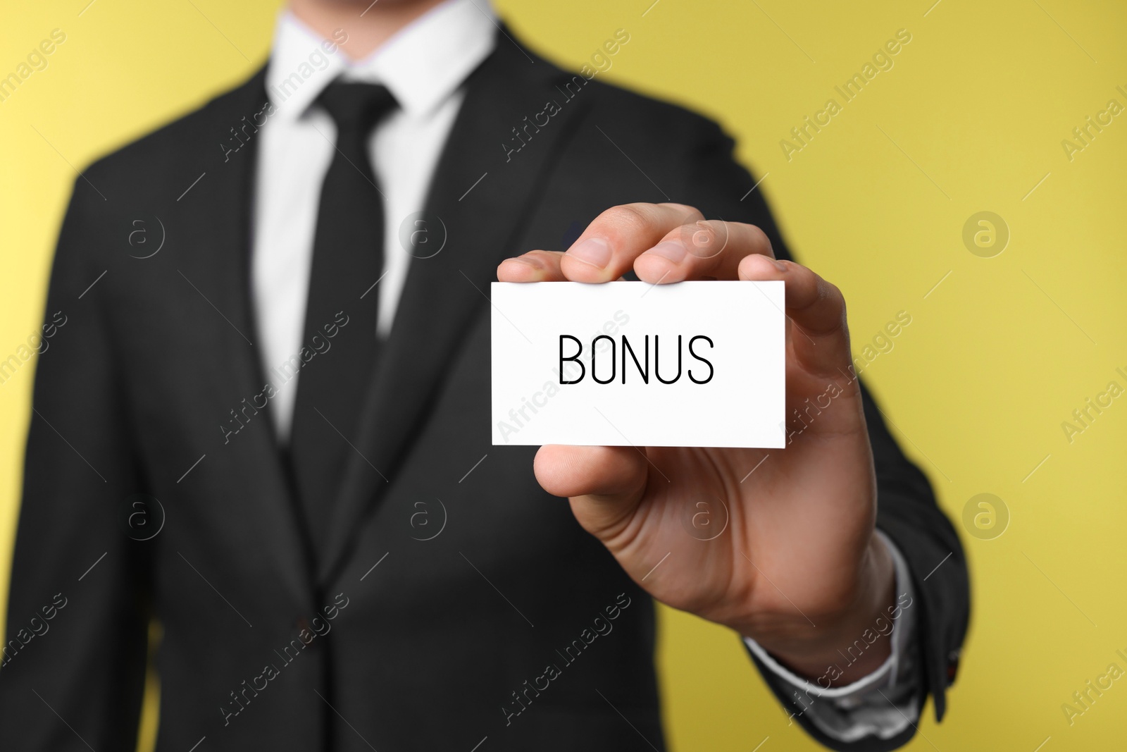 Businessman showing card with word bonus on yellow background, closeup Image of Businessman showing card with word bonus on yellow background, closeup