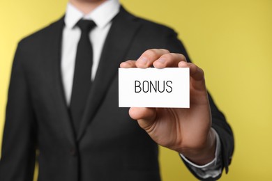 Image of Businessman showing card with word bonus on yellow background, closeup