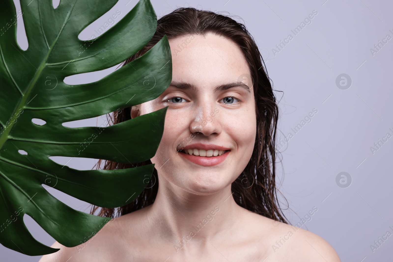 Portrait of smiling woman with natural skin complexion and monstera leaf on grey background, closeup Photo of Portrait of smiling woman with natural skin complexion and monstera leaf on grey background, closeup