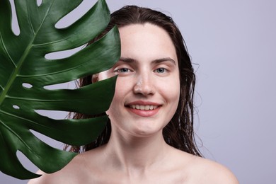 Photo of Portrait of smiling woman with natural skin complexion and monstera leaf on grey background, closeup