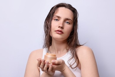Photo of Portrait of beautiful woman with jar of skincare product on light grey background, closeup