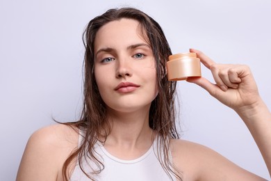 Photo of Portrait of beautiful woman with jar of skincare product on light grey background, closeup