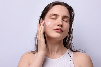 Photo of Beautiful woman applying skincare product onto her face on light grey background, closeup