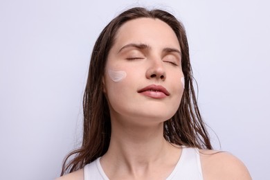 Photo of Beautiful woman with skincare product on her face against light grey background, closeup