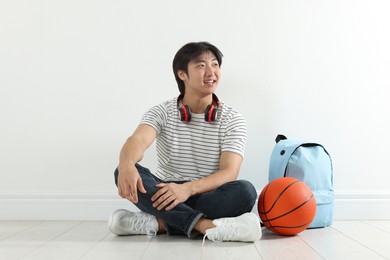 Photo of Happy student with basketball ball and backpack on floor indoors