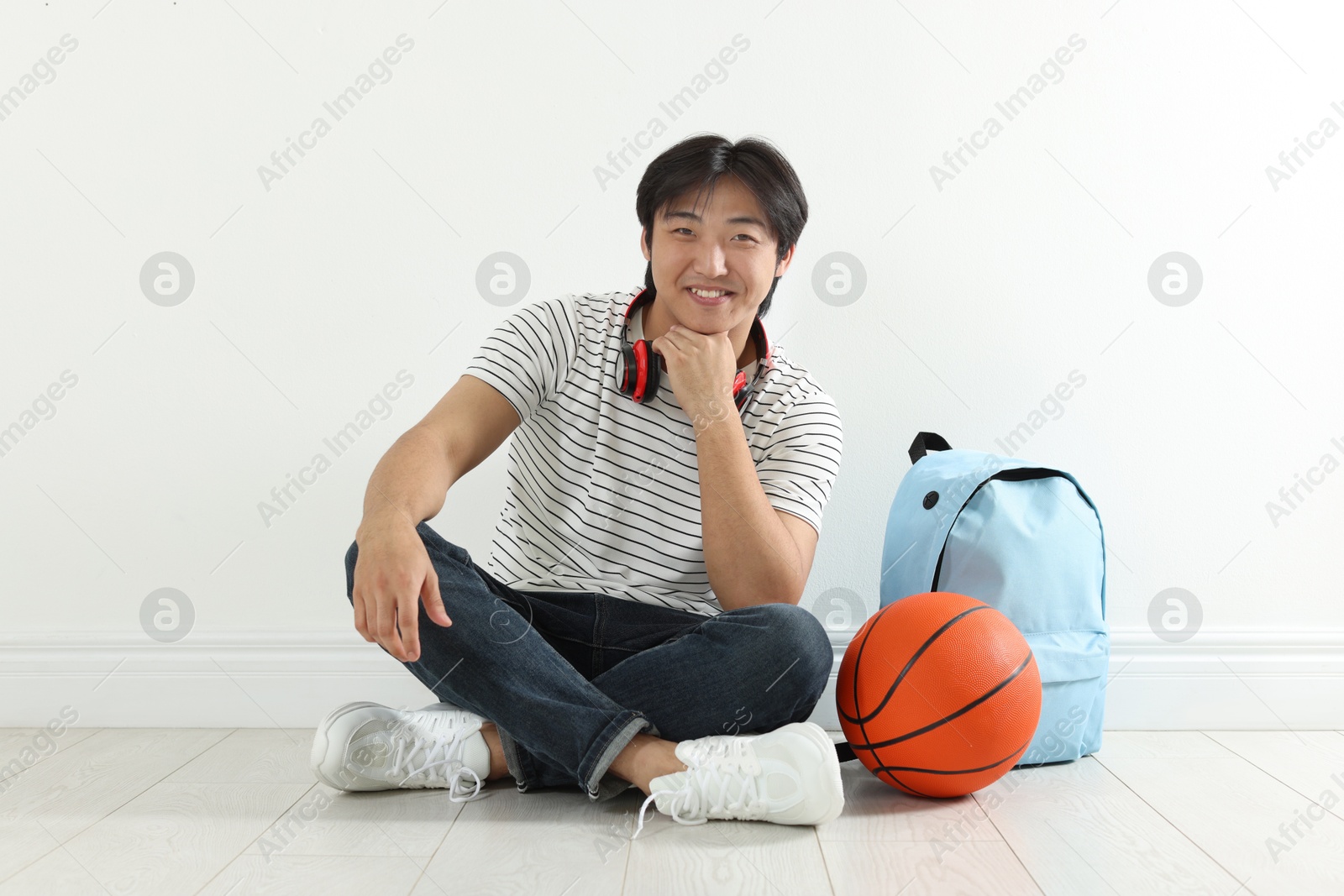 Happy student with basketball ball and backpack on floor indoors Photo of Happy student with basketball ball and backpack on floor indoors