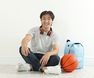 Photo of Happy student with basketball ball and backpack on floor indoors
