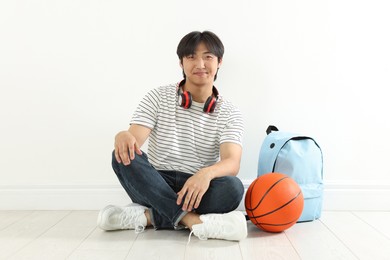 Photo of Student with basketball ball and backpack on floor indoors