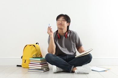 Photo of Student with notebook and pen studying on floor indoors