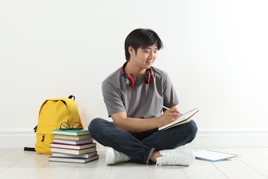 Photo of Student with notebook and pen studying on floor indoors