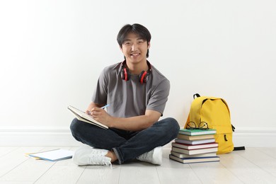 Photo of Student with notebook and pen studying on floor indoors