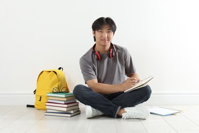 Photo of Student with notebook and pen studying on floor indoors