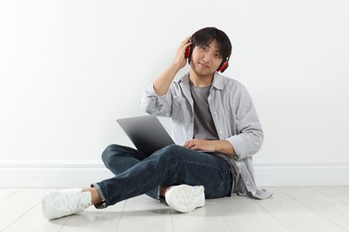 Photo of Student with headphones and laptop studying on floor indoors